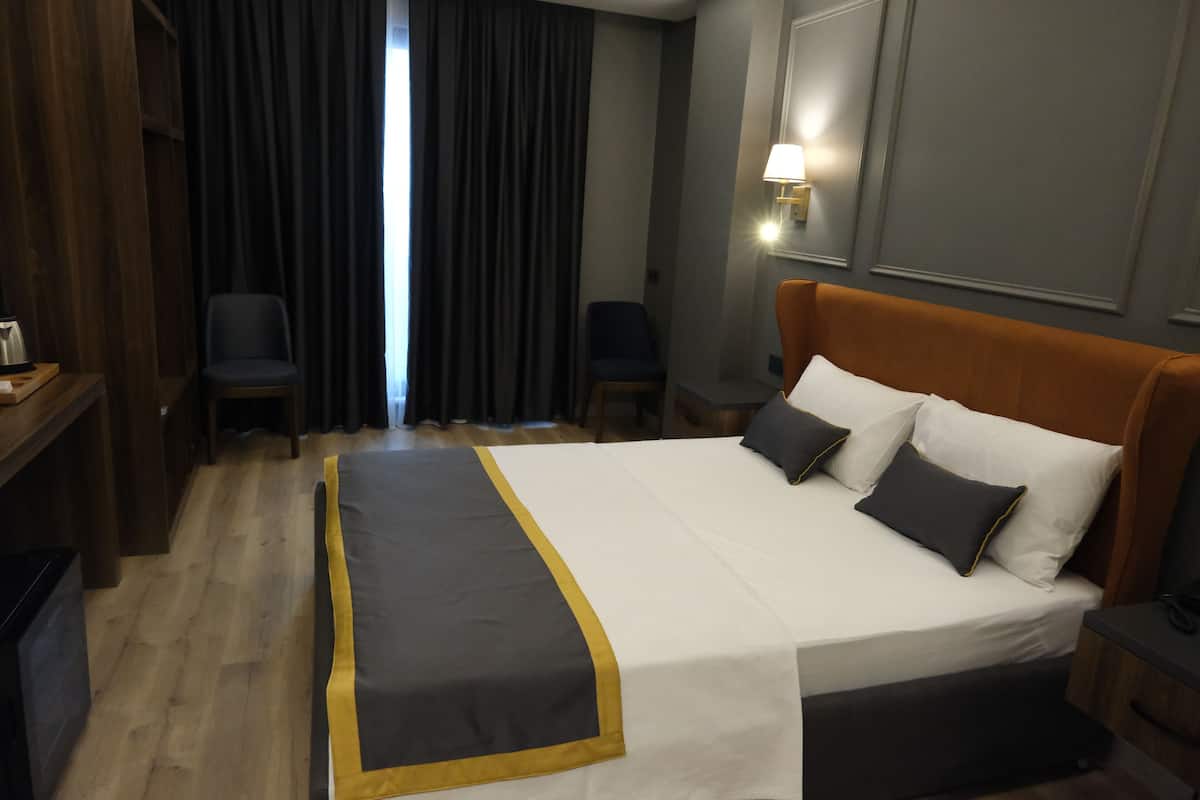 Habitación de hotel con cama, escritorio, silla y ventana con cortinas.