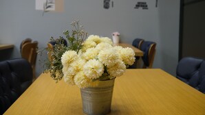 A wooden table with a metal bucket containing white flowers. - The Pearl Airport Hotel (Arnavutköy)