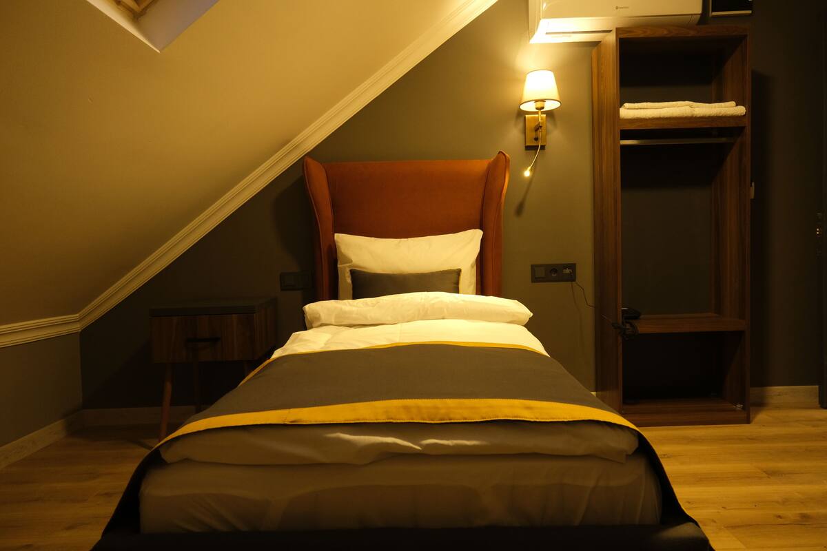 Una cama individual con cabecera, una mesita de noche, una lámpara de pared y un armario de madera.