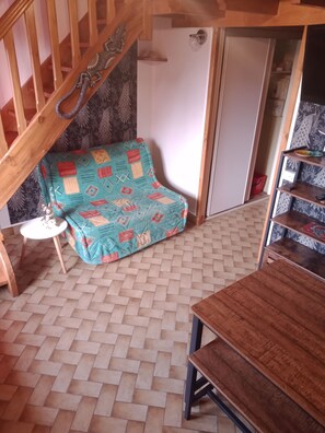 Une pièce avec un canapé à motifs, une table en bois, un parquet à chevrons, un escalier en bois et une armoire aux portes décorées.