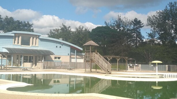 Una piscina con cubierta de madera, un pabellón y un edificio con techo curvo.