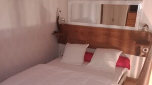 Un dormitorio con estructura de cama de madera, ropa de cama blanca y un espejo sobre la cama.