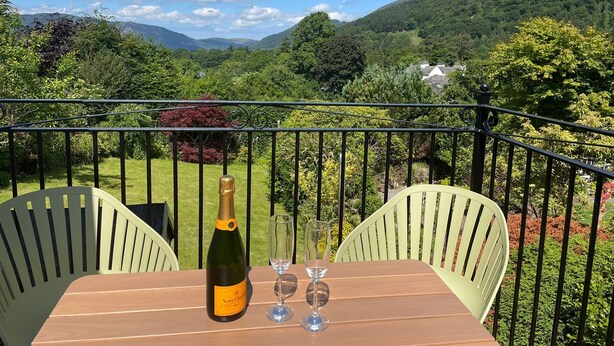 Un balcón con una mesa, dos sillas, una botella de Veuve Clicquot champagne y dos copas.