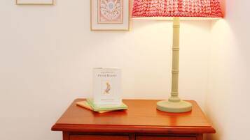 A wooden nightstand with a lamp, a book titled "The Tale of Peter Rabbit," and framed pictures on the wall.
