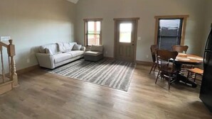 Un loft spacieux avec un plafond haut, un escalier en bois, un canapé blanc, une table à manger avec des chaises et deux fenêtres aux cadres triangulaires.
