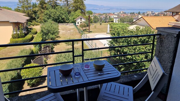 A balcony with a table and chairs, overlooking a residential area with houses and a distant view of the sea. - L'haumana (Thonon-les-Bains)