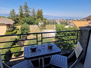 A balcony with a table and chairs, overlooking a residential area with houses and a distant view of the sea.