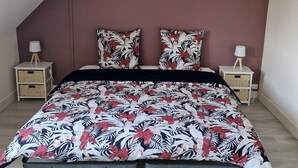A bedroom with a sloped ceiling, a bed with a floral bedspread, two nightstands with lamps, and wicker baskets. - L'haumana (Thonon-les-Bains)