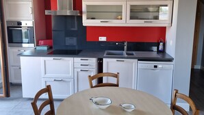 A modern kitchen with white cabinets, a red accent wall, and a dining area with a round table and four chairs. - L'haumana (Thonon-les-Bains)