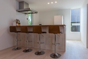 A modern kitchen with a bar area, four bar stools, and a large window.