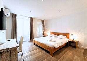 A hotel room with a wooden bed, a desk, a chair, and a TV. - Viva Riviera 3 bedrooms Natural Loft Luxury Collection (Cannes)
