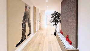 A hallway with a wooden floor, a large abstract painting on the left, a potted plant, and a textured wall on the right. - Viva Riviera 3 bedrooms Natural Loft Luxury Collection (Cannes)
