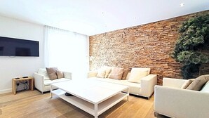 A modern living room with a white sofa set, a white coffee table, and a brick-patterned accent wall. - Viva Riviera 3 bedrooms Natural Loft Luxury Collection (Cannes)