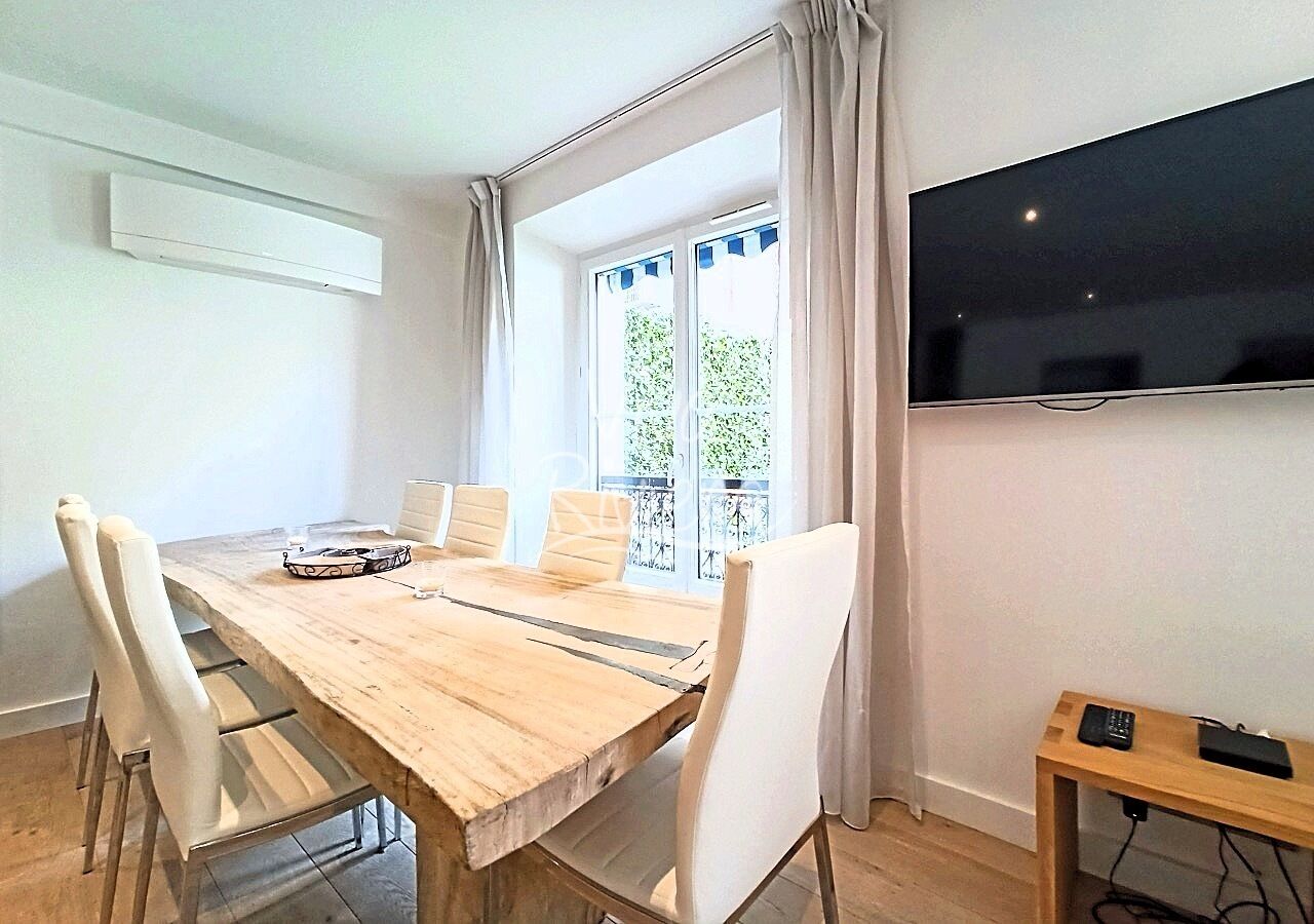 A dining area with a wooden table, white chairs, a TV on the wall, and a balcony with a view.