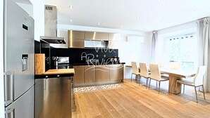 A modern kitchen with stainless steel appliances, a wooden countertop, and a dining area with a large table and chairs. - Viva Riviera 3 bedrooms Natural Loft Luxury Collection (Cannes)