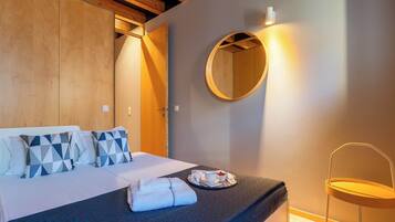 Cama bem arrumada com edredom escuro, almofadas estampadas com padrão geométrico e bandeja com xícara e comida.
