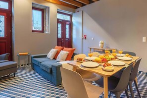 A cozy room with a blue sofa, a dining table set with plates, glasses, and fruit, and a patterned floor.