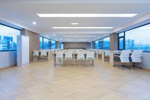 Un salón de conferencias con una larga mesa, sillas y grandes ventanales que ofrecen vistas a la ciudad.