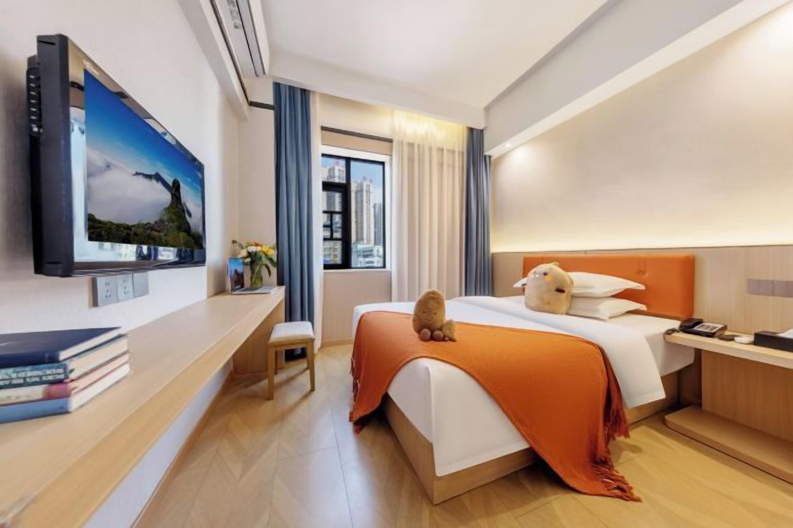 A hotel room with a bed, a TV, a desk, and a window with curtains.
