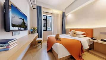 A hotel room with a bed, a TV, a desk, and a window with curtains.