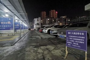 Ein Parkplatz bei Nacht mit in Reihen geparkten Autos, einem Schild mit Text und Gebäuden im Hintergrund.