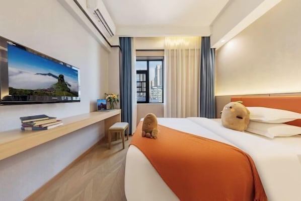 A hotel room with a bed, a TV on the wall, a window with curtains, and a view of a cityscape.