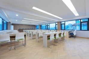 A spacious conference room with multiple tables and chairs, large windows with a city view, and modern lighting fixtures.