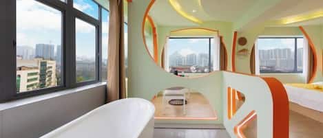 A modern bathroom with a large bathtub, a small seating area, and large windows offering city views.