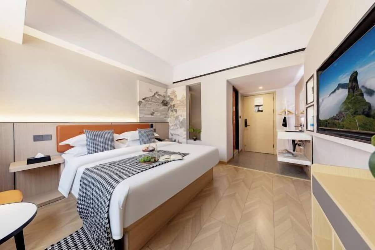 Moderni hotellihuone, jossa on suuri sänky, yöpöytä, työpöytä ja näkymä ulos.