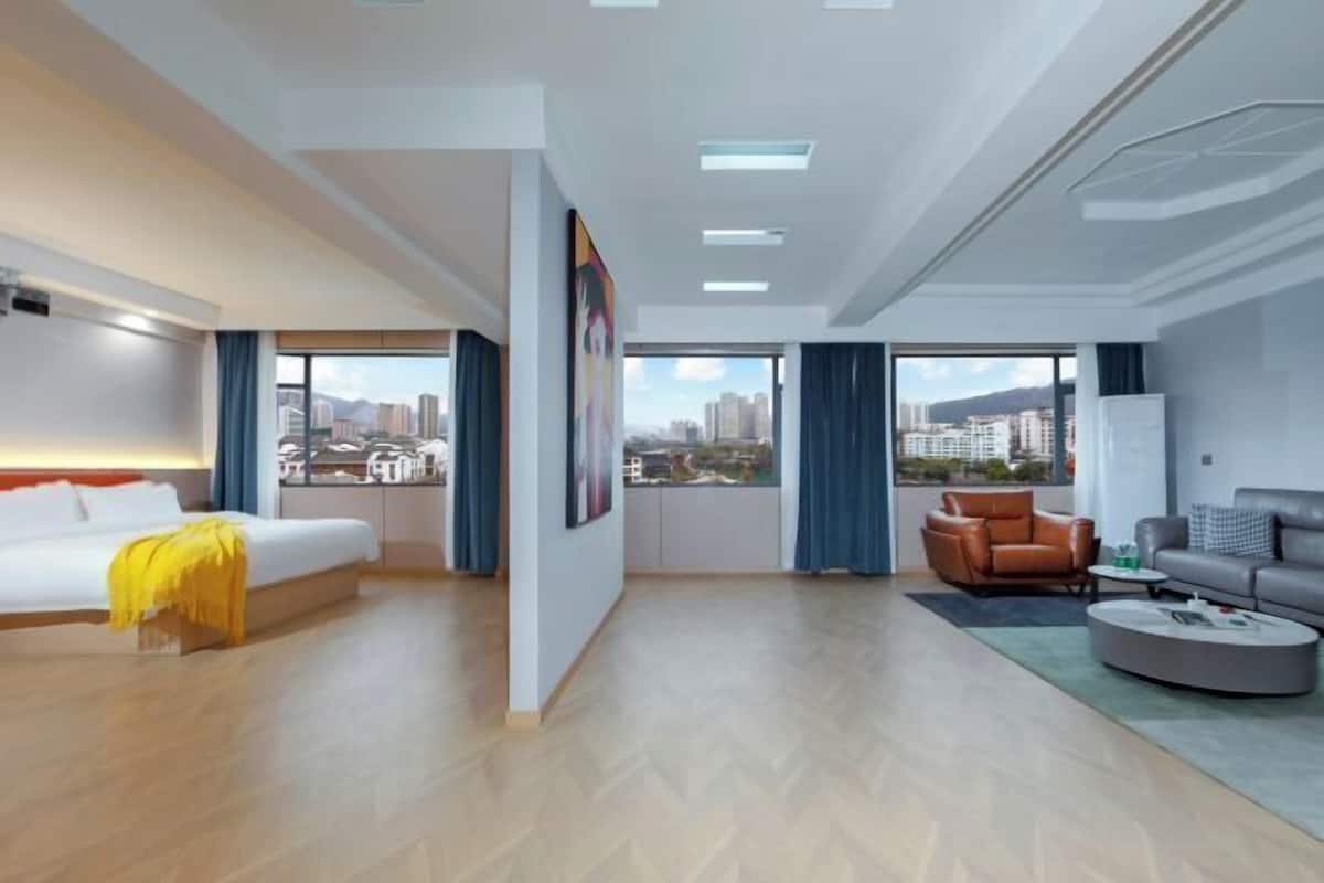 Moderni hotellihuone, jossa on sänky, sohva, sohvapöytä ja näkymä kaupunkiin.