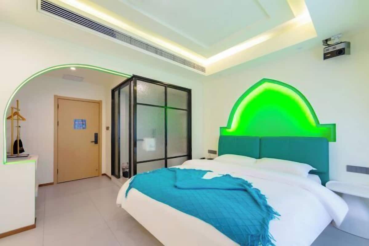 Moderni hotellihuone, jossa on sänky, työpöytä ja lasiseinä.