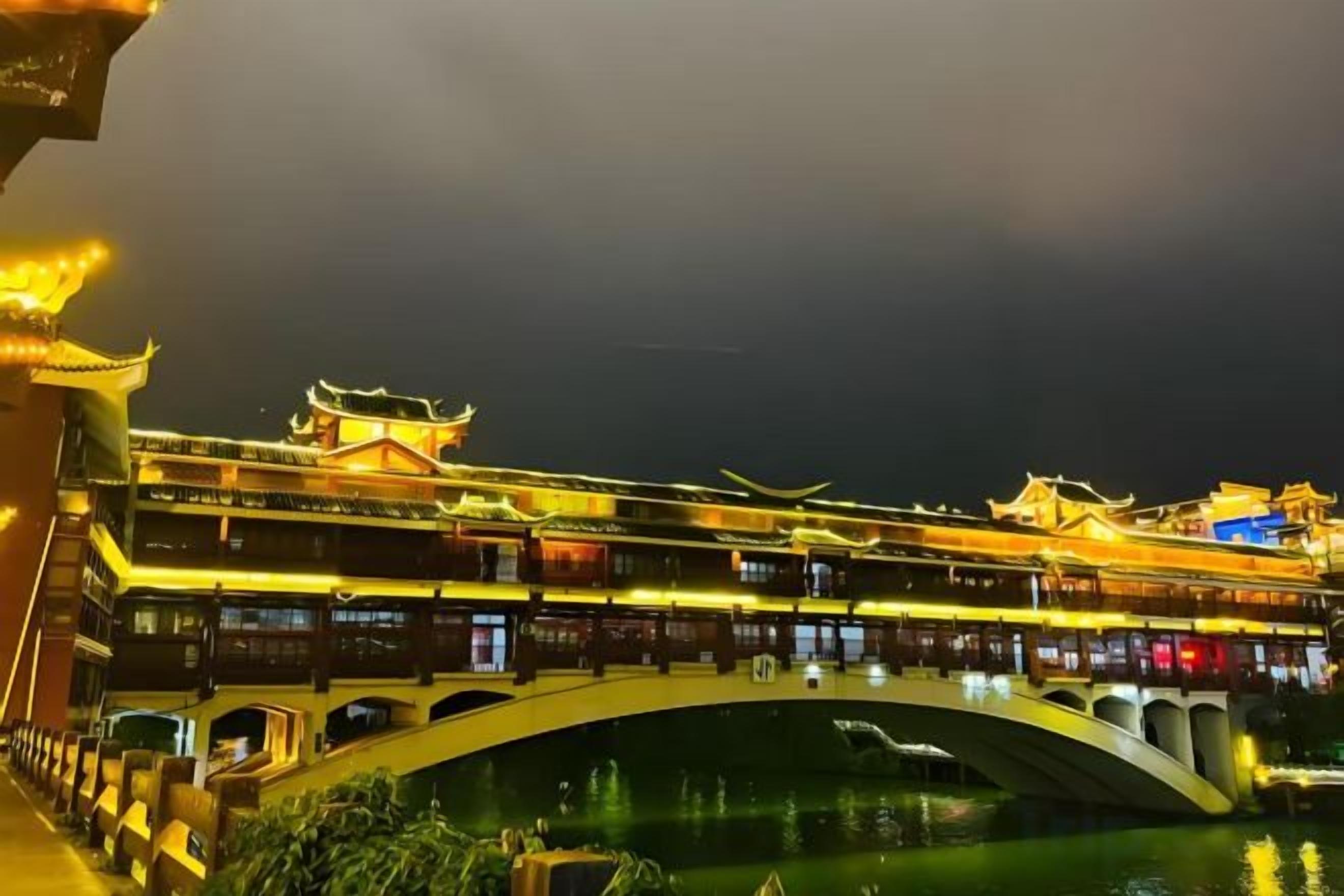 Un edificio tradicional con un puente sobre el agua, con varios niveles e iluminado con luces artificiales.