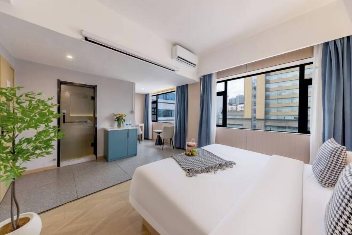 Moderni hotellihuone, jossa on suuri sänky, työpöytä, pieni keittiönurkkaus ja näkymä kaupunkiin.