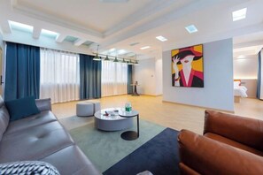Una sala de estar moderna con sofá, reposapiés, una mesa de centro y una obra de arte en la pared.