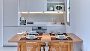 A modern kitchen with white cabinetry, a wooden dining table set for four, and a built-in microwave above the counter. - Perivoli Luxury Homes, Paros, Greece (Paros)