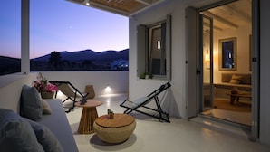 A modern outdoor patio with a view of the mountains, a sofa, a table, and a chair. - Perivoli Luxury Homes, Paros, Greece (Paros)
