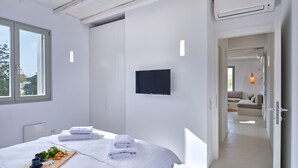 A modern hotel room with a large bed, a flat-screen TV mounted on the wall, and a breakfast tray on the bed. - Perivoli Luxury Homes, Paros, Greece (Paros)