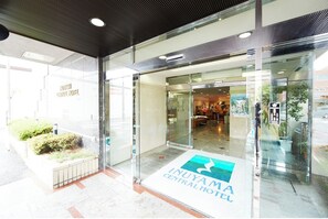 Enter the Inuyama Central Hotel through its glass door, offering a glimpse into the reception area with a counter and seating.