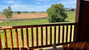 A wooden deck with chairs, overlooking a fenced field and a tree.
