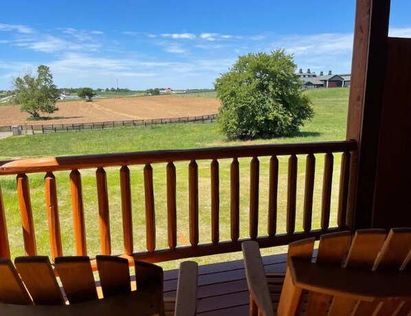Una terraza de madera con sillas, con vistas a un campo cercado y un árbol.