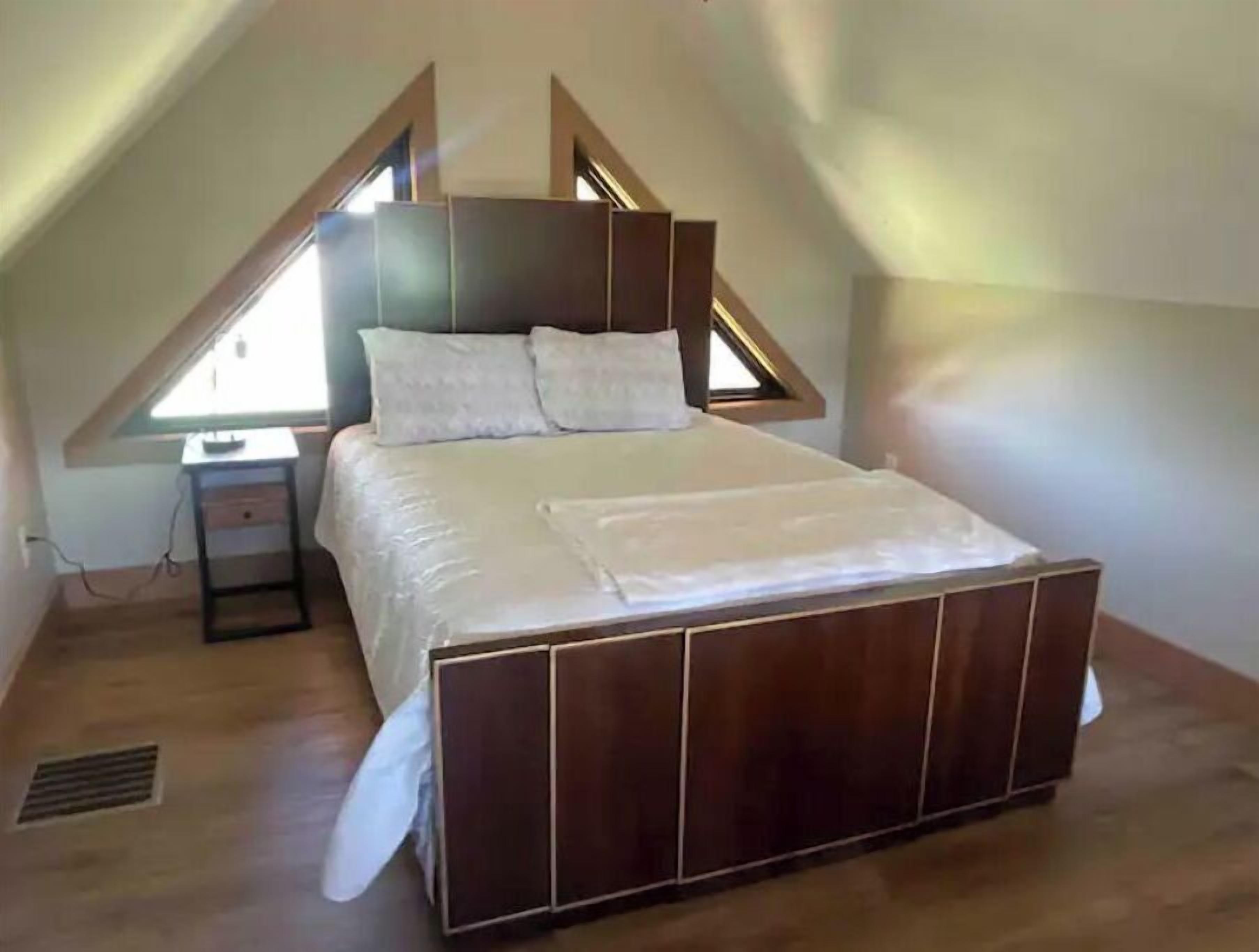 A bedroom with a sloped ceiling, a wooden bed frame, a bedside table, and a window.