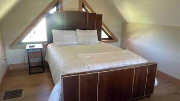 A bedroom with a sloped ceiling, a wooden bed frame, a bedside table, and a window.