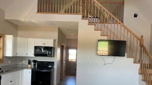 A spacious kitchen with white cabinets, a microwave, and a stove. A wooden staircase leads to a second floor.