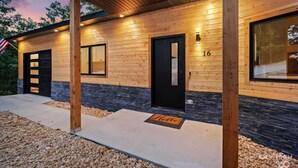 A modern log cabin with a black door, a window, and a welcome mat.