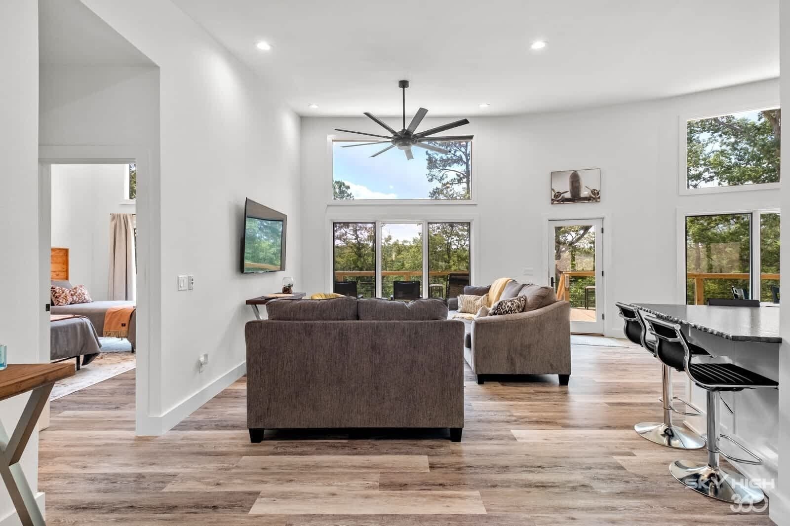 A spacious living room with a large ceiling fan, a dining area with a bar, and a view of the outdoors.