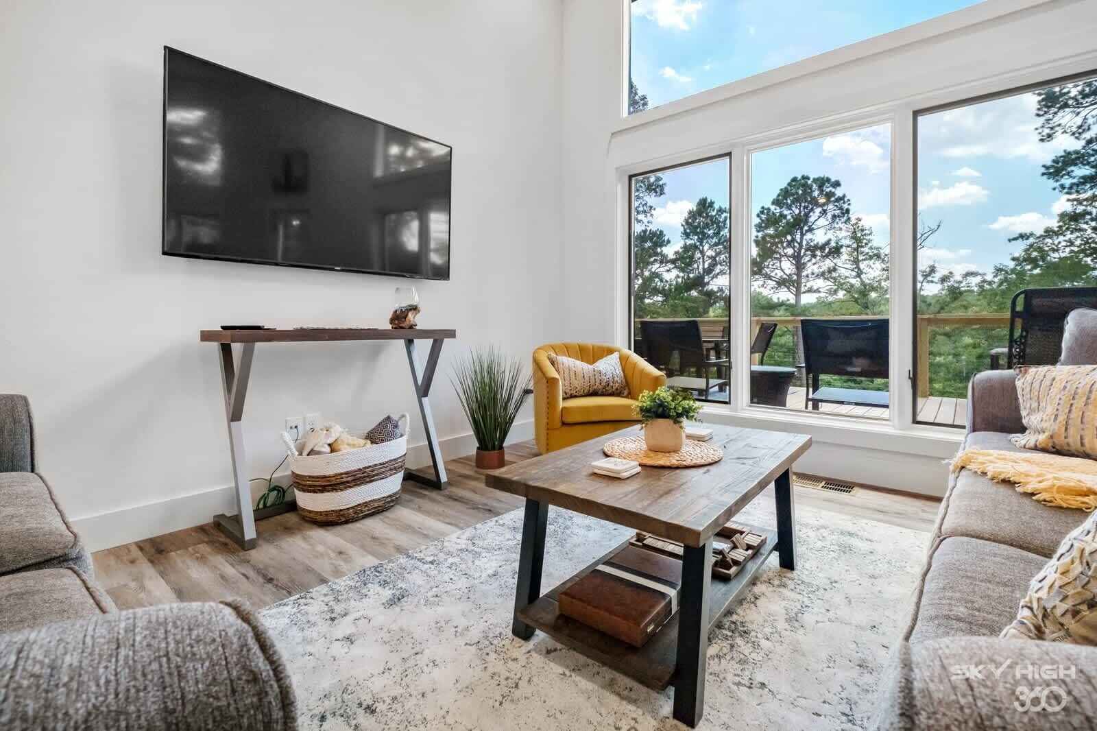 A modern living room with a large TV, a sofa, a coffee table, and a view of the outdoors.
