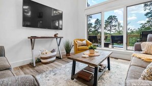 A modern living room with a large TV, a sofa, a coffee table, and a view of the outdoors.