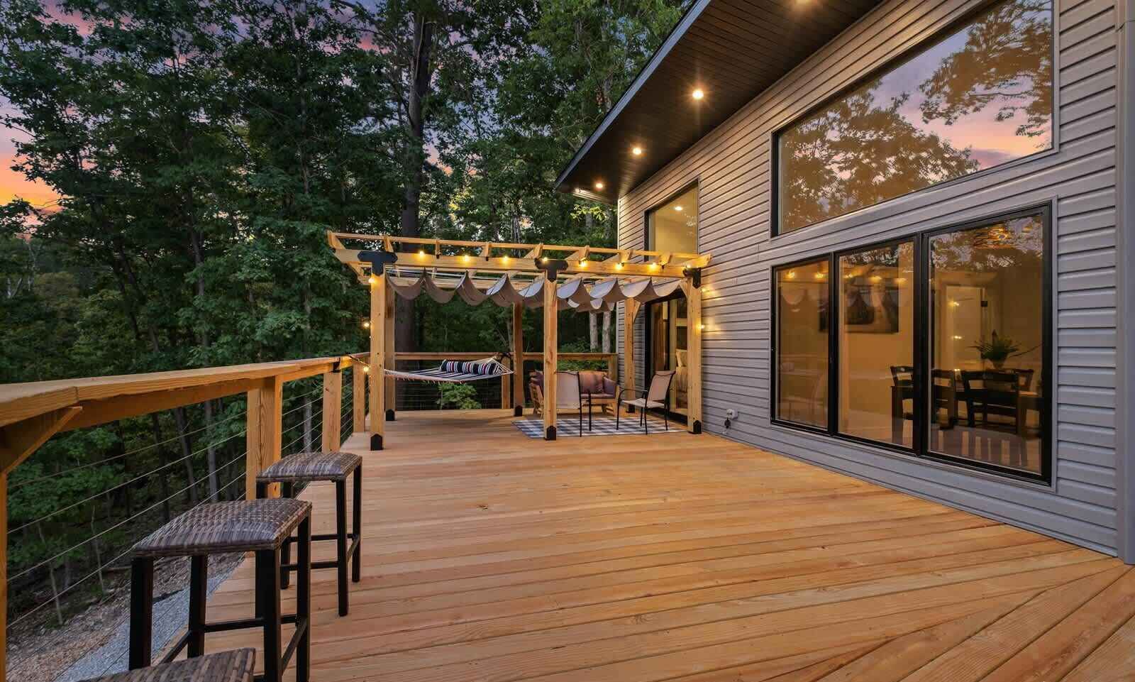 A wooden deck with outdoor seating, a pergola with string lights, and a large sliding glass door to a room.