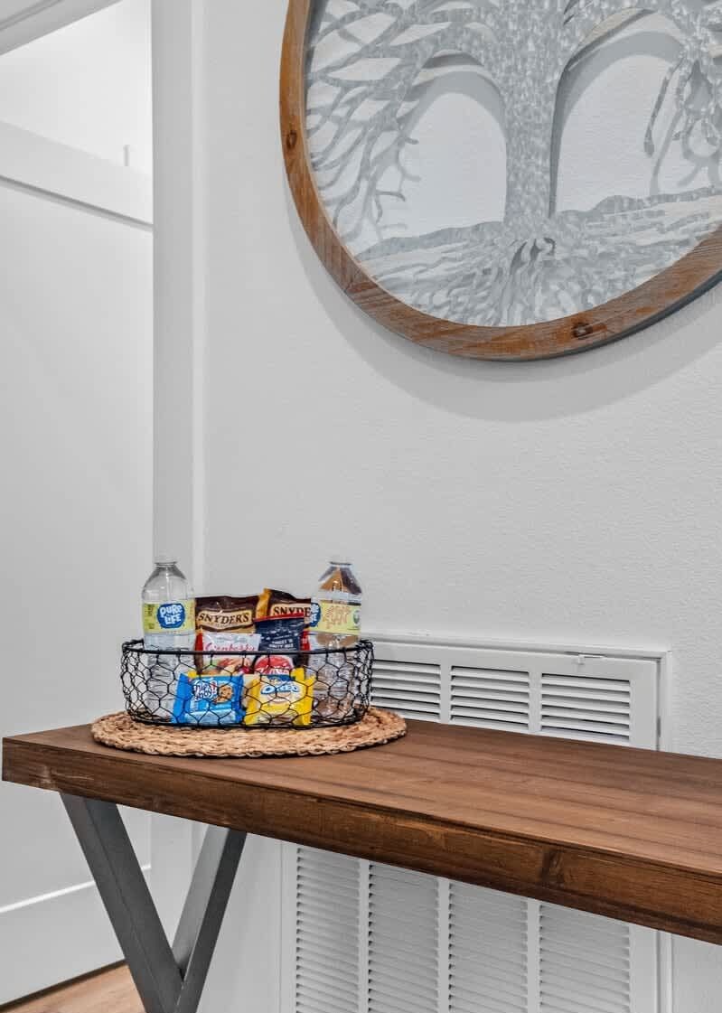 A wooden table with a basket containing snacks and drinks, a wall-mounted tree silhouette, and a white radiator.