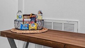 A wooden table with a basket containing snacks and drinks, a wall-mounted tree silhouette, and a white radiator.